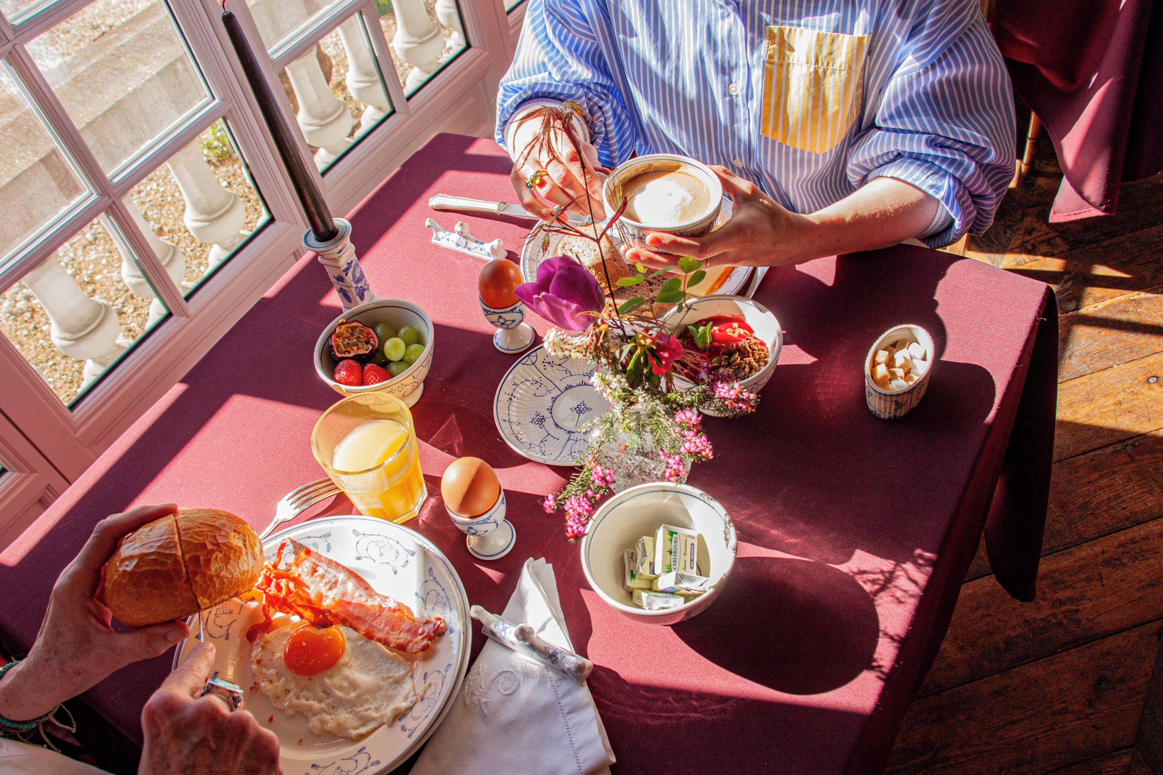 Una mesa de comedor con alimentos para el desayuno, un jarrón con flores y una ventana con vistas.