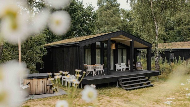 A wooden cabin with a deck, outdoor seating, and a hot tub.