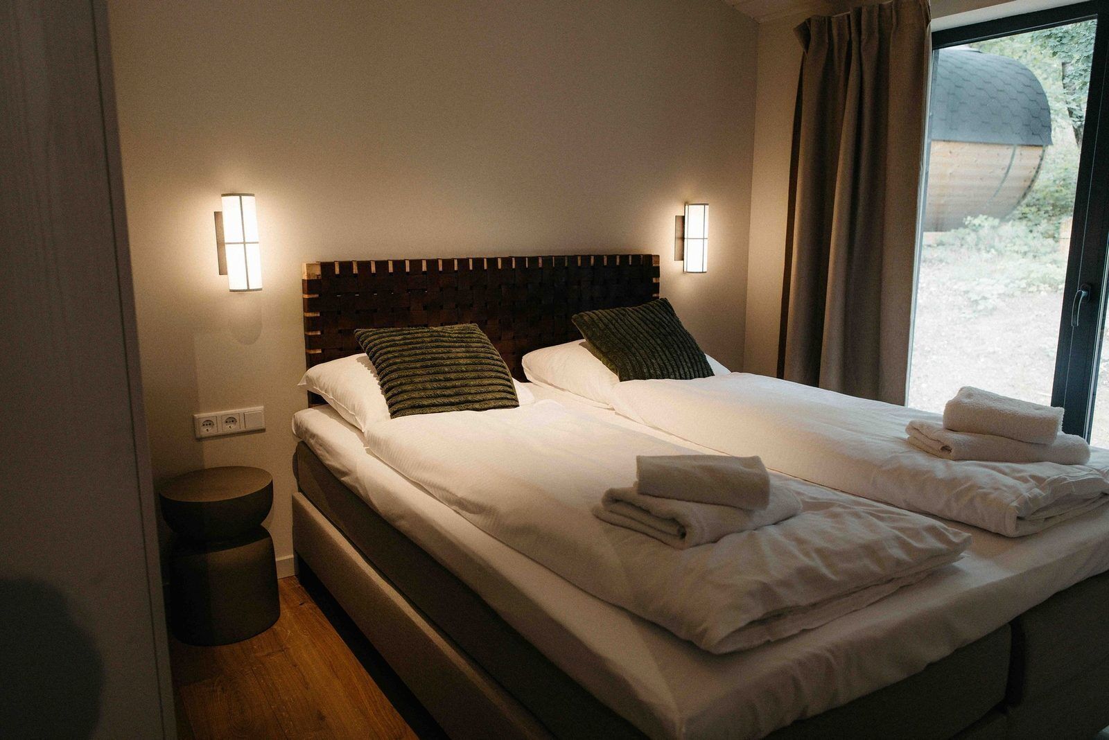 A neatly made bed with pillows, a bedside table, and a window with curtains.