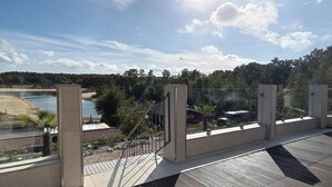 A balcony with a view of a beach, a body of water, and a forested area.