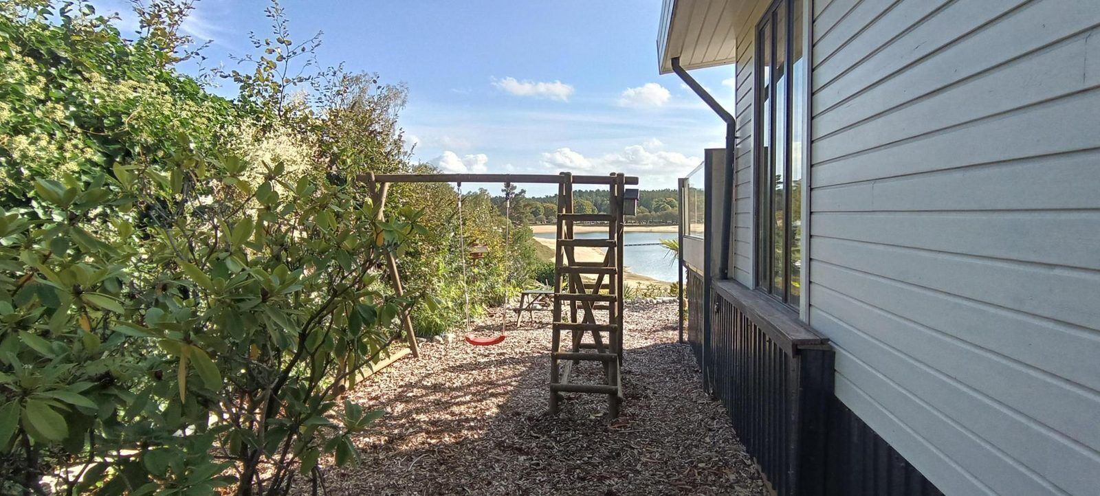 A wooden swing set and a ladder in a backyard with a view of a body of water.
