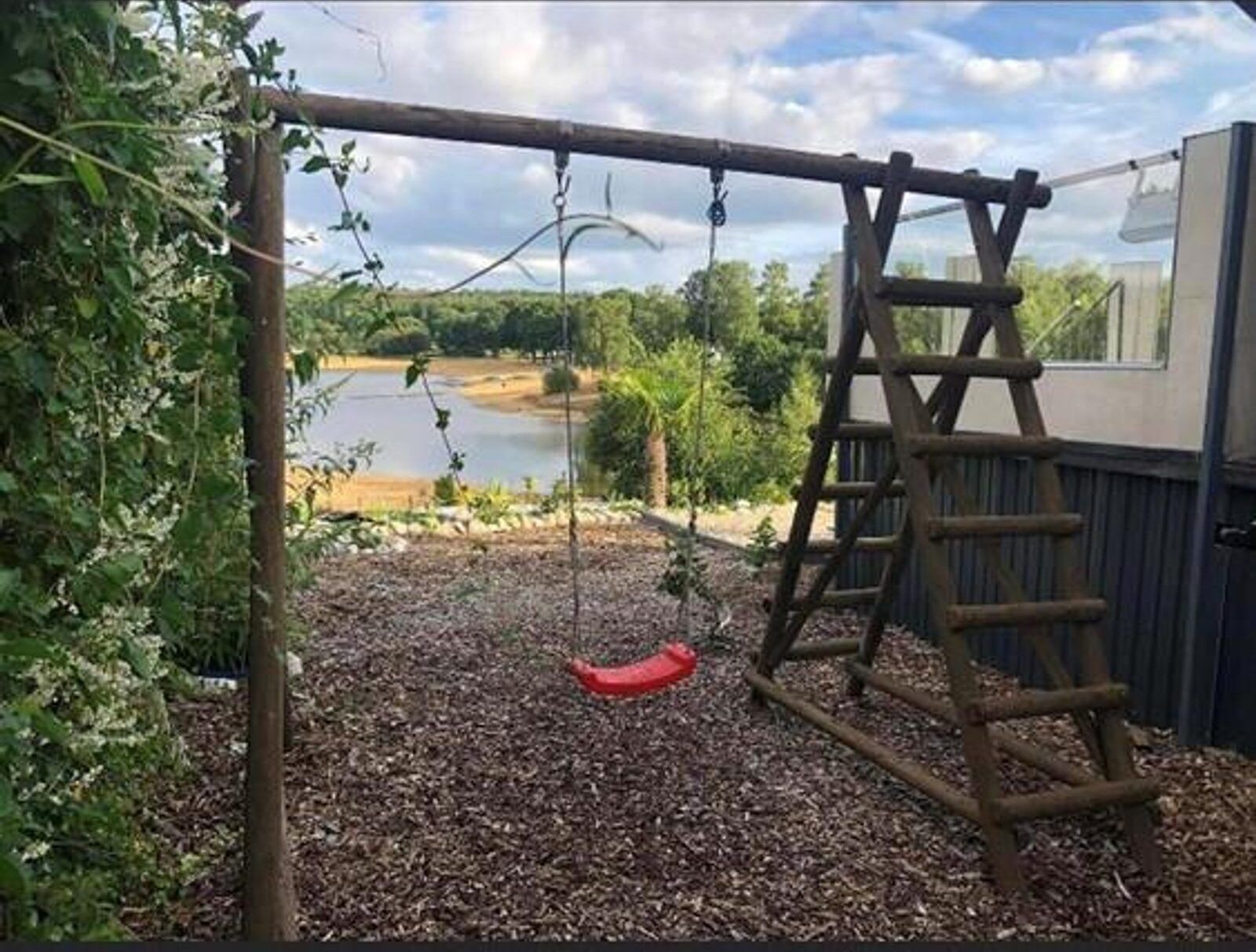 Un portique en bois et une échelle dans un jardin avec un étang et des arbres.