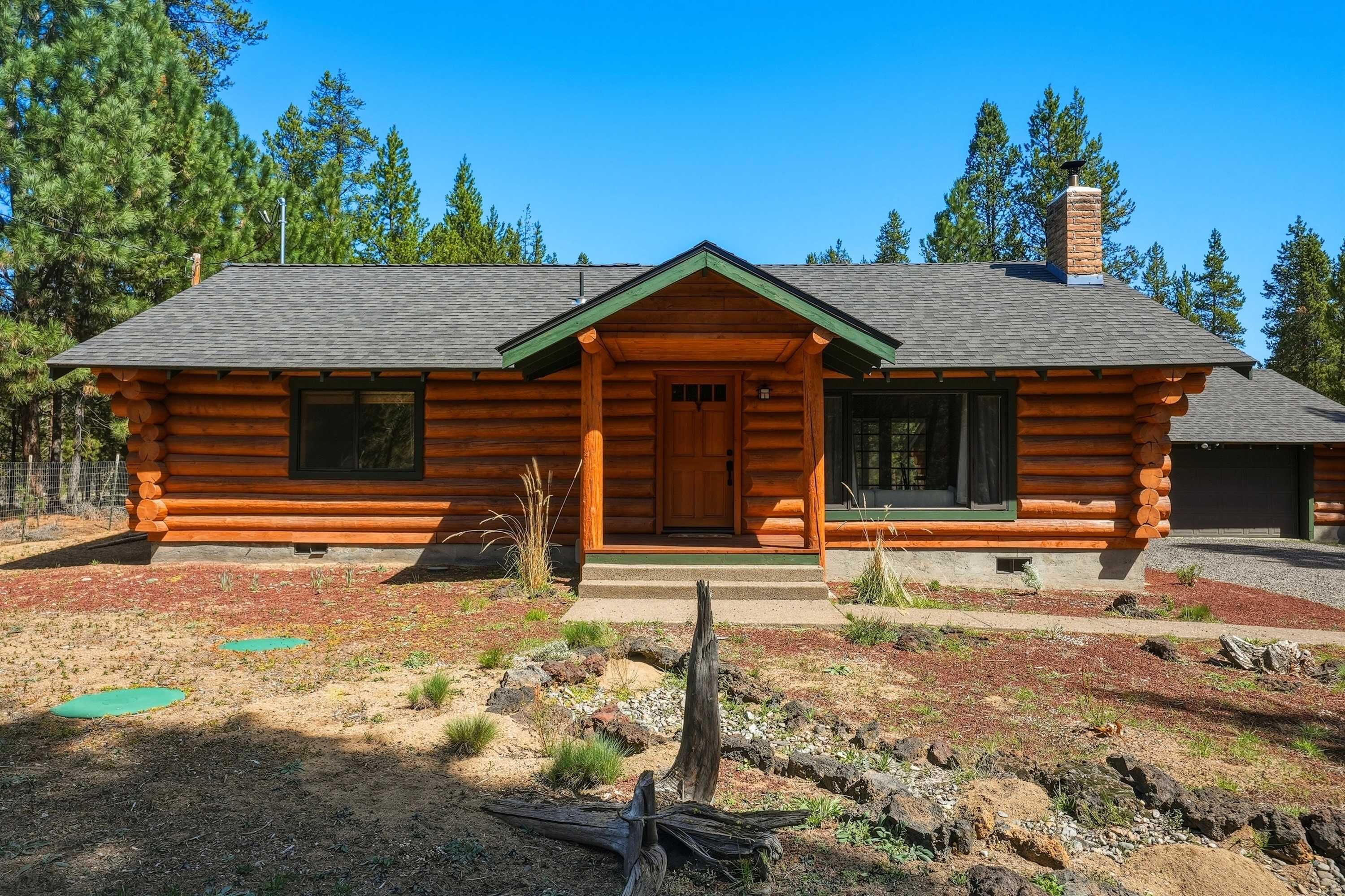 A log cabin with a front porch, a chimney, and a clear view of the surrounding forest.
