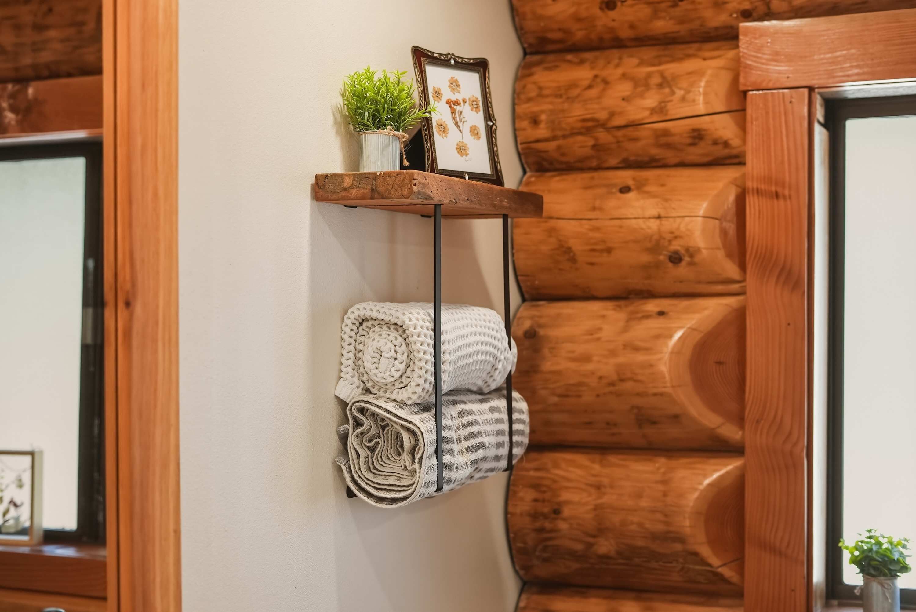 A wooden wall with a shelf holding a potted plant, a framed picture, and rolled towels.