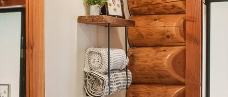 A wooden wall with a shelf holding a potted plant, a framed picture, and rolled towels.