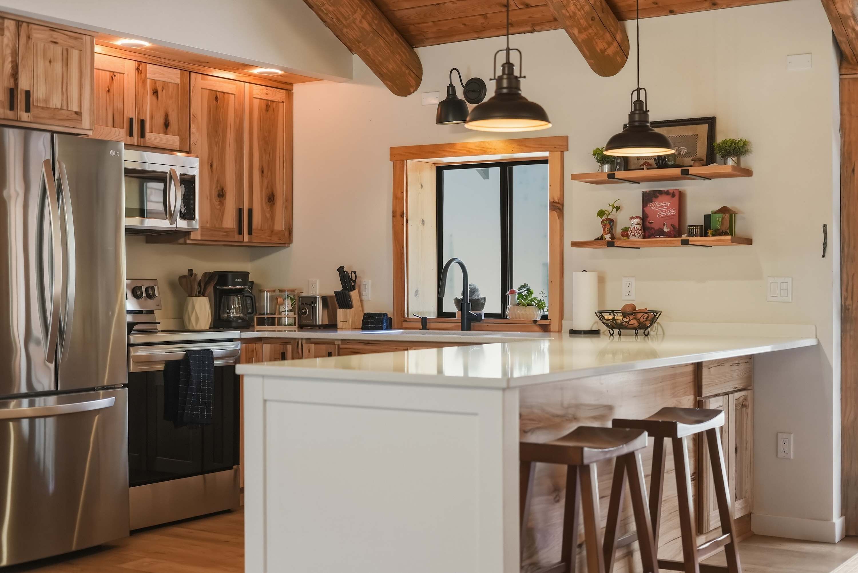 A modern kitchen with wooden cabinets, stainless steel appliances, a large island with stools, and pendant lighting.