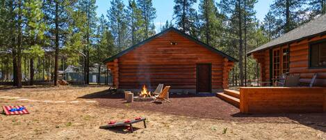 A log cabin with a fire pit, outdoor seating, and a view of tall pine trees.