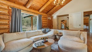 Interior de una cabaña de madera con techo de madera, una mesa redonda para café, un sofá modular y una araña.