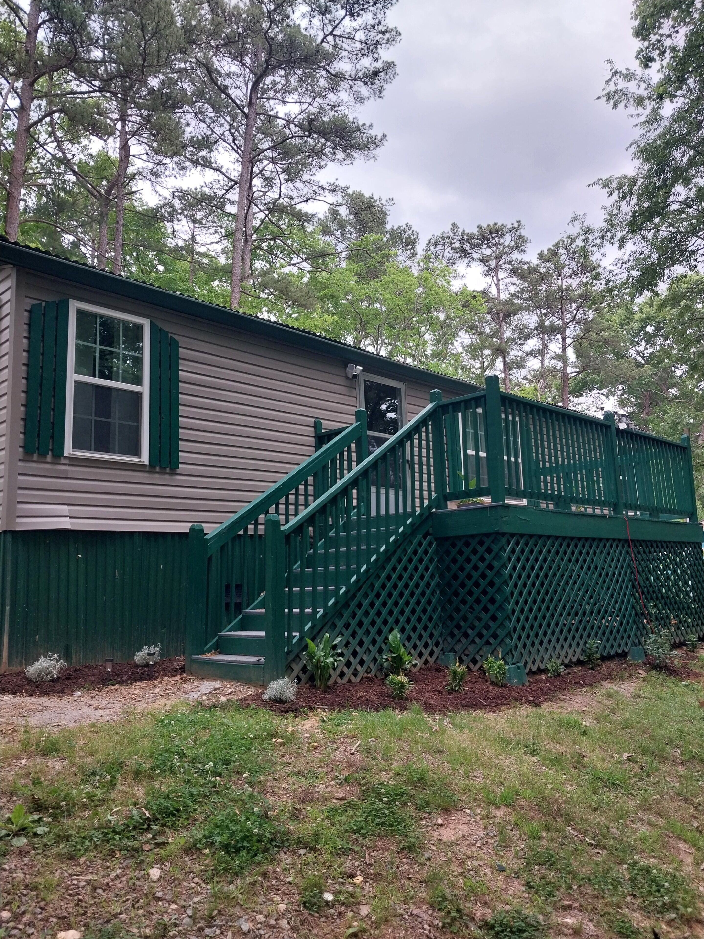 A single-story house with a green exterior, a visible window with shutters, and a small porch area.