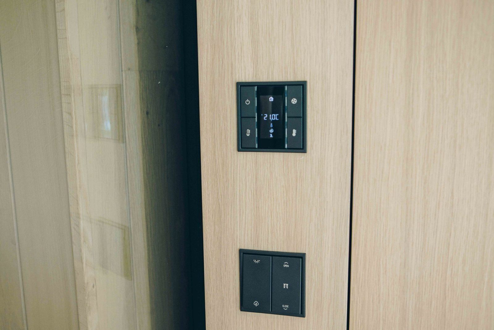 Een houten paneel met twee zwarte bedieningspanelen, waarvan er een een digitaal scherm en knoppen heeft, en de ander eenvoudige open/close-indicatoren.