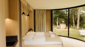 A modern bedroom with a large bed, a view of the outdoors, and a wooden wall.
