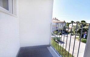 A balcony with a metal railing, a clear view of a parking area, and a building with a red-tiled roof in the background. - Comfortable Apartment in Umag (Umag)