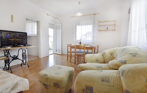 Ein Wohnzimmer mit Fernseher, Esstisch und Sofa.