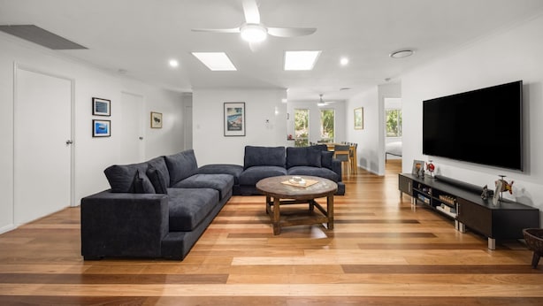 A modern living room with a sectional sofa, a round coffee table, a flat-screen TV, and a ceiling fan. - Serene Mount Coolum Escape Near the Beach (Sunshine Coast)