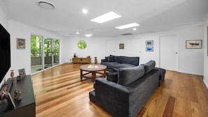 A spacious living room with a large gray sectional sofa, a wooden coffee table, and a wooden floor. - Serene Mount Coolum Escape Near the Beach (Sunshine Coast)