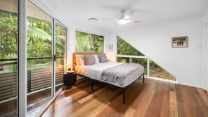 A bedroom with a bed, a nightstand, a ceiling fan, and a large window with a view of greenery. - Serene Mount Coolum Escape Near the Beach (Sunshine Coast)