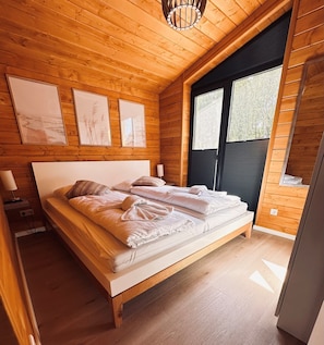 Un dormitorio de cabaña de madera con una cama, mesitas de noche y obras de arte enmarcadas en la pared.