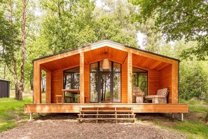 A wooden cabin with a porch, large windows, and a table and chairs. - Wilsumer Berge Resort - Forest House Scandi (Wilsum)