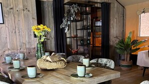 A dining area with a wooden table, floral upholstered chairs, and a bookshelf. - Wilsumer Berge Resort - Glamfield Lodge Premium (Wilsum)