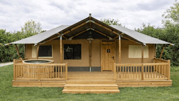 A wooden cabin with a porch, a hot tub, and a door. - Wilsumer Berge Resort - Glamfield Lodge Premium (Wilsum)