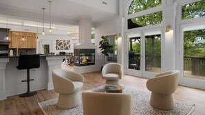 A spacious living area with a fireplace, comfortable seating, and large windows offering a view of the outdoors. - Modern Marble - Big Canoe, GA (Jasper)