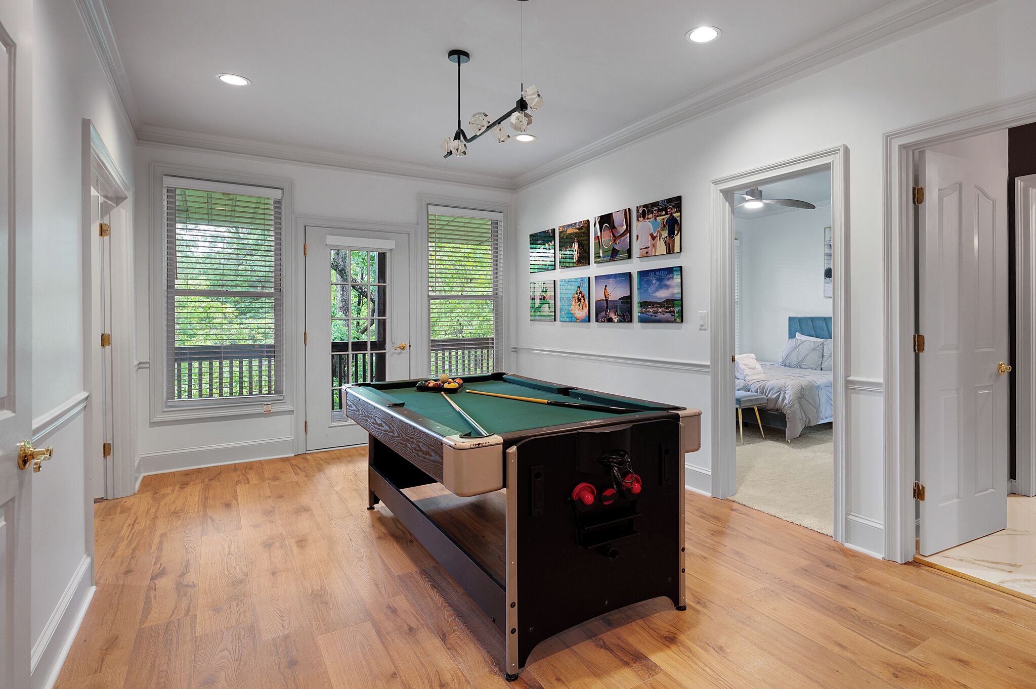 Une table de billard dans une pièce dotée d’un plancher en bois, de murs blancs et de grandes fenêtres.