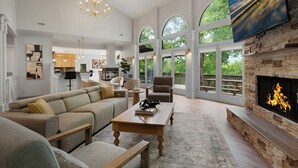 A spacious living room with a fireplace, large windows, and a modern chandelier. - Modern Marble - Big Canoe, GA (Jasper)