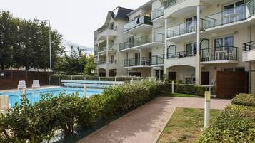 Un edificio residencial de varios pisos con balcones, piscina y un jardín bien cuidado.