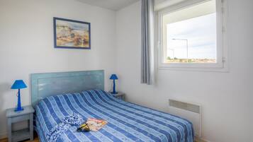 Un dormitorio con una cama, mesitas de noche, una lámpara, una ventana y un cuadro en la pared.