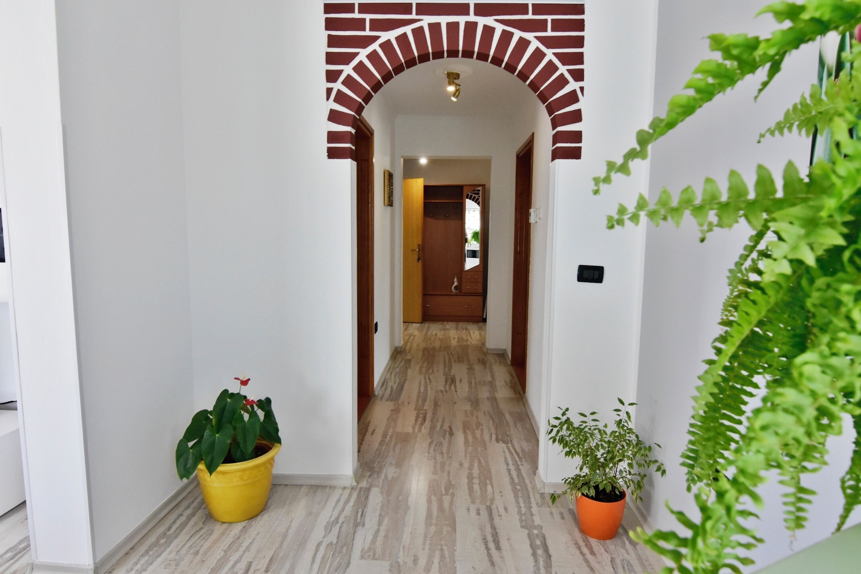 A hallway with a brick archway, potted plants, and a wooden door at the end.