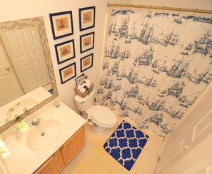 A bathroom with a white sink, a toilet, framed pictures on the wall, and a shower curtain with a nautical print. - Quaint Condo Short Drive to Rehoboth Beach! (Rehoboth Beach)