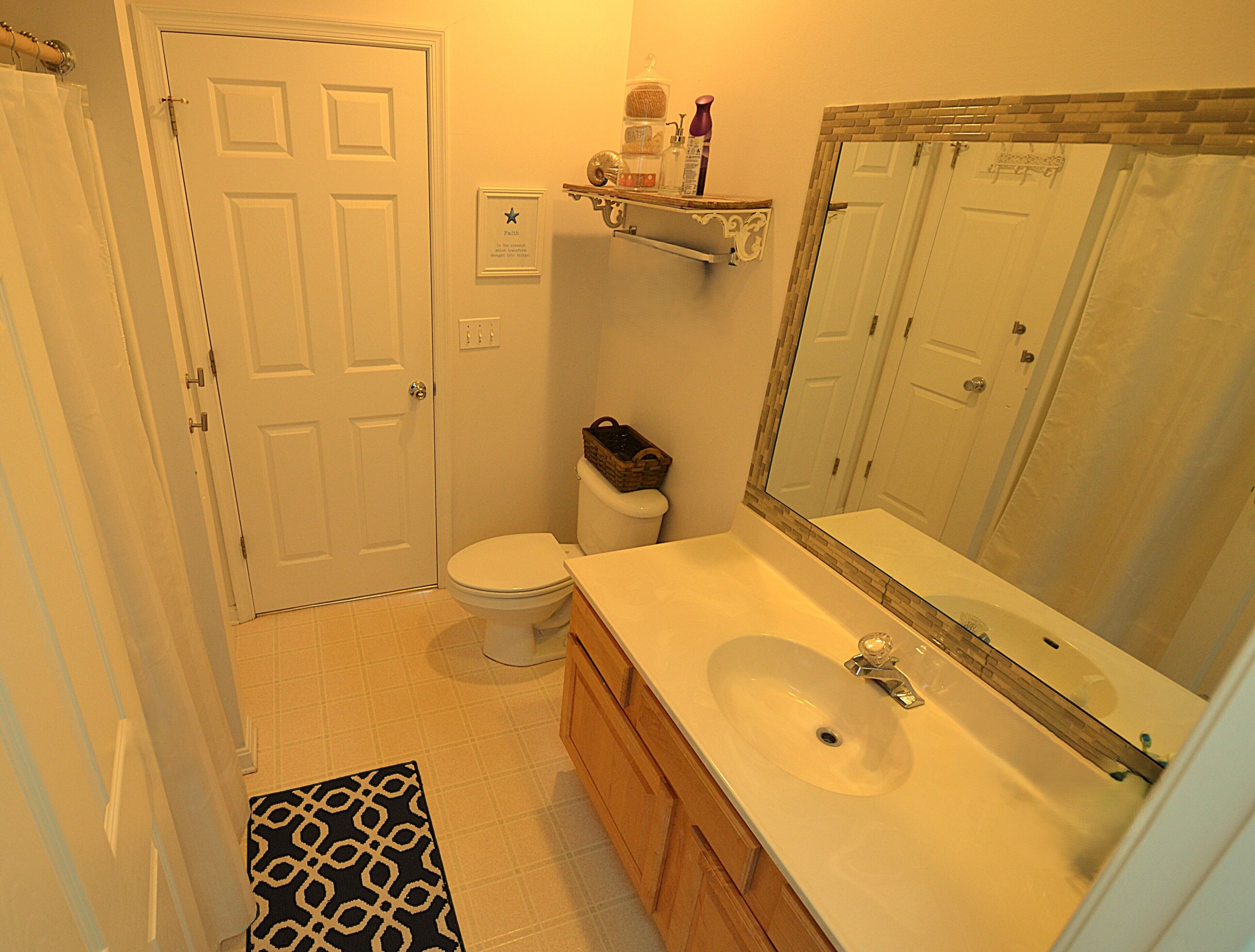 A bathroom with a toilet, sink, mirror, and a patterned rug.