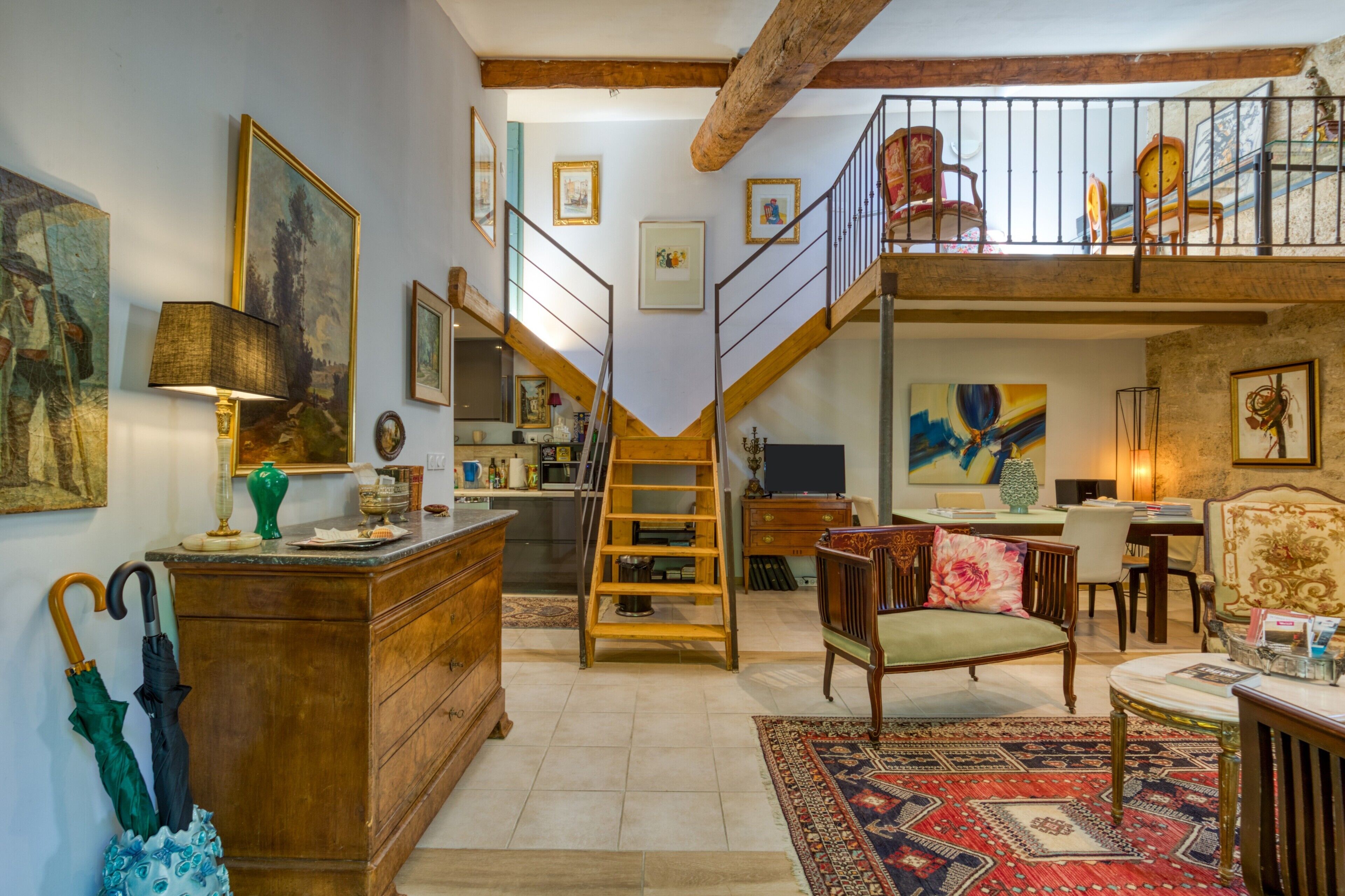 A spacious loft with a wooden staircase, a dining area, and a loft bedroom with a balcony.