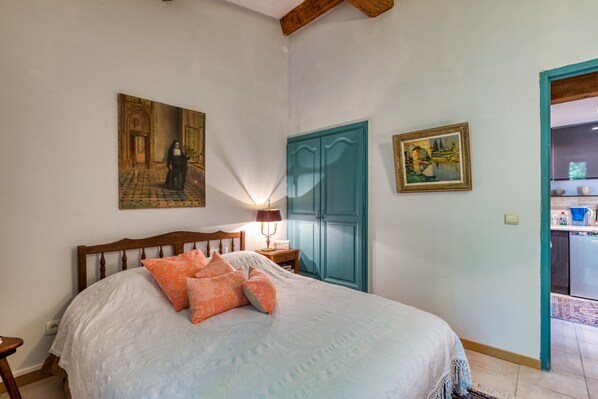 Camera da letto con un letto, un comodino, una lampada, una porta e due quadri appesi al muro.