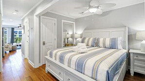 Een slaapkamer met een bed, een plafondventilator, een nachtkastje en een raam.