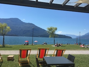 Ein Sitzbereich im Freien mit Stühlen und Tischen, Blick auf einen See und Berge im Hintergrund.