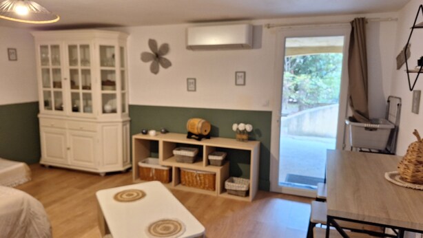 A room with a wooden floor, a white cabinet, a table with chairs, and a window with curtains. - Provencal village between Aix en Provence and Cassis (Fuveau)