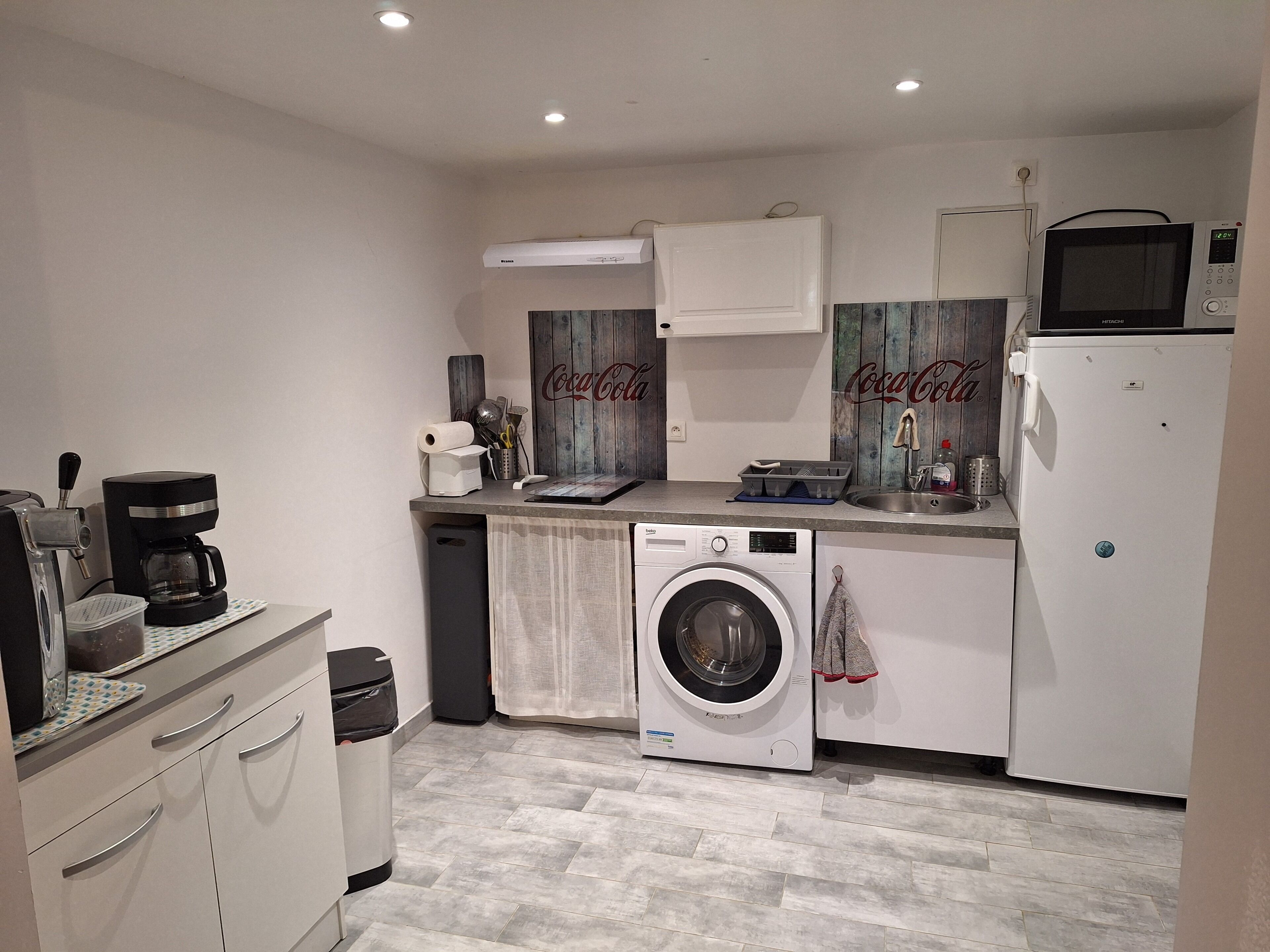 Een functionele keuken met een wasmachine, magnetron en koffiezetapparaat.