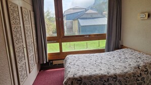 A room with a bed, a window with curtains, a wooden ceiling, and a wall with decorative panels.