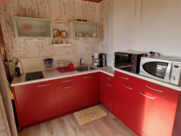 Une cuisine de taille réduite avec des placards rouges, un four à micro-ondes, un grille-pain et une machine à café.