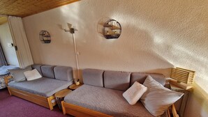 A cozy room with a wooden sofa, a small table, and a wall-mounted shelf.