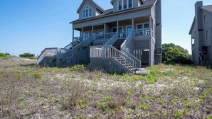 Una casa costiera con un ampio portico, diverse scale e vista sulla spiaggia.
