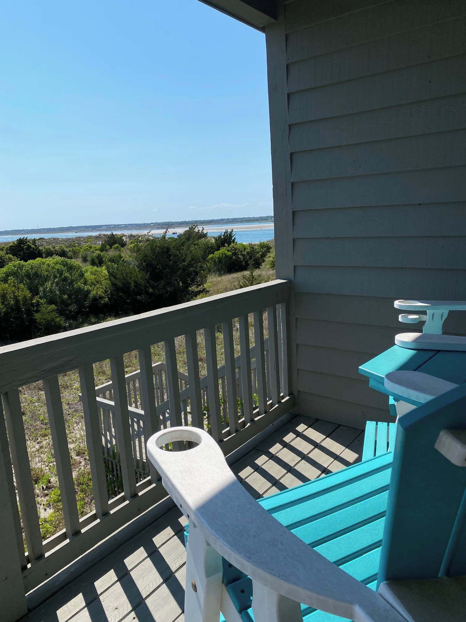 A covered outdoor area with a view of the beach, a white railing, and blue outdoor furniture.