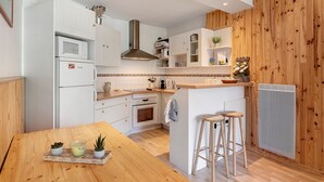 A compact kitchen with white cabinetry, a central island, a built-in stove, and a wooden accent wall. - Superb Apartment with Mountain View at the Foot of the Slopes (Villard-de-Lans)