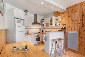 A compact kitchen with white cabinetry, a central island, a built-in stove, and a wooden accent wall. - Superb Apartment with Mountain View at the Foot of the Slopes (Villard-de-Lans)