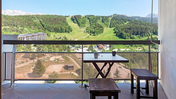 A balcony with a table and chairs, overlooking a mountainous landscape with a golf course. - Superb Apartment with Mountain View at the Foot of the Slopes (Villard-de-Lans)