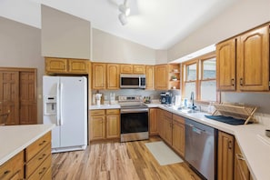 Una cocina con armarios de madera, refrigerador, microondas, horno y lavavajillas.