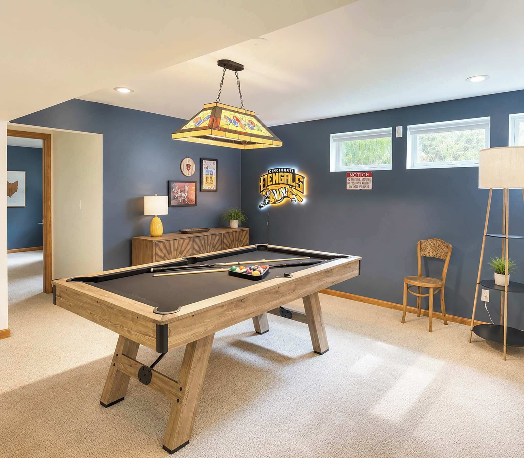 A pool table in a room with a dark blue wall, a ceiling light fixture, and a window.