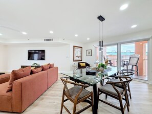 A modern living room with a glass dining table, wooden chairs, a sofa, and a flat-screen TV. - Recently renovated BEACH condo, tons of amenities (Indian Shores)