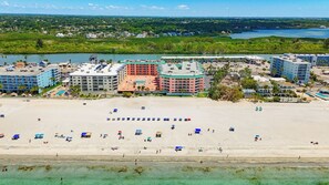 A coastal hotel with multiple buildings, a beach with umbrellas, and a view of the ocean and greenery in the background. - Recently renovated BEACH condo, tons of amenities (Indian Shores)
